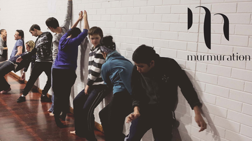 murmuration dance logo letter m with dancers against a wall in workshop setting