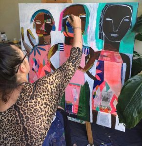 Angie Goto sits with her back to the camera and is painting at the easel