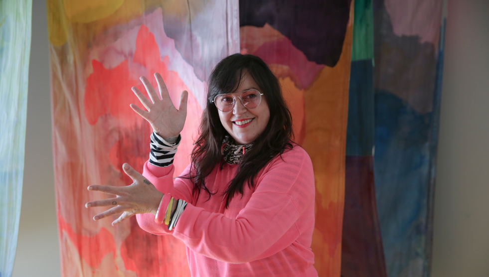 History: A woman is standing in front of a painting while making an Auslan sign
