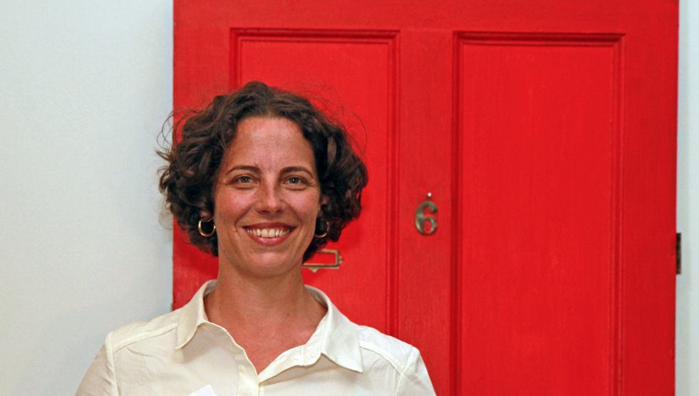 Kate Matairavula: woman in a white shirt is standing against a white wall and red door