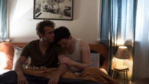 Two young men are sitting on a bed and holding each other