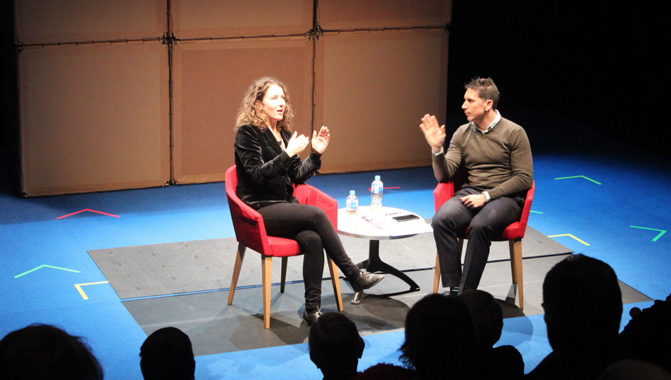 Jodee Mundy and Alex Jones are sitting on chairs on a stage. They are signing in Auslan. Photo by Sophie Clausen