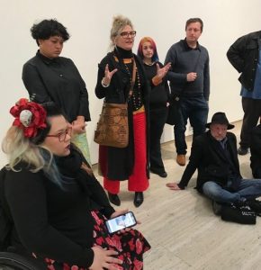 A group of artists is standing in a group and a woman is talking to them and motioning with her hands