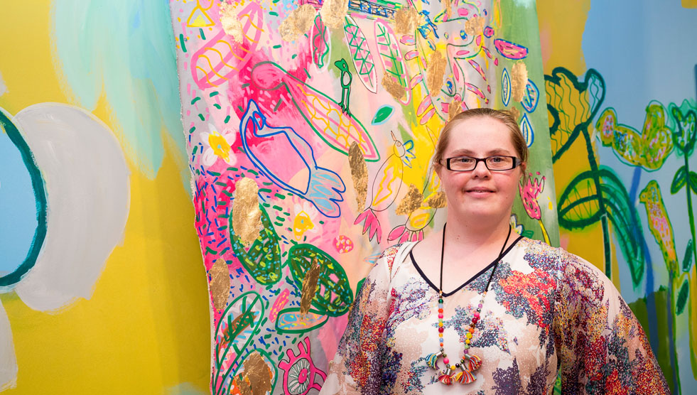 National Arts and Disability Strategy: A woman is standing in front of a large and colourful artwork