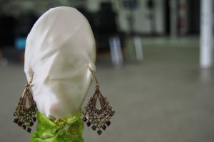 A sculpture with a white cloth head, a green top and dangling earings