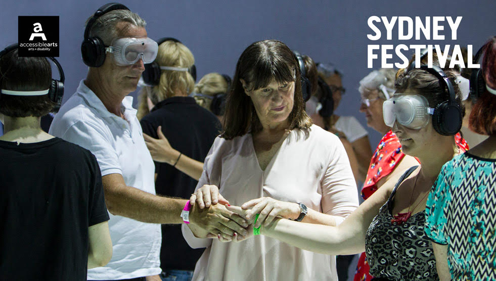 Disability Programming Initiative: Two people are wearing masks and have their hands joined. A woman is standing between them and has her hands placed on their joined hands.